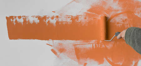 Wall painting by male hand with paint roller. Painting the apartment, renovation with orange paint. Baner.の写真素材