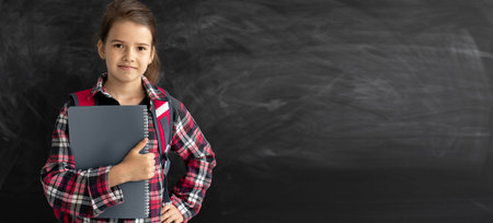 caucasian girl student in the classroom near the chalk board. He holds a notebook in his hands and...
