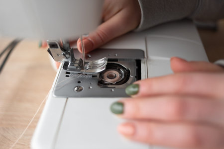 The seamstress replaces the bobbin in the sewing machine, close-up of female hands with manicure....