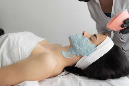 Beautiful young woman at the reception at the beautician, alginate mask, the process of applying to the face, side view. Close-up. Cosmetic procedure in a modern beauty salon. personal hygiene.の写真素材