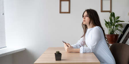 Young calm caucasian young business woman sitting at the table holding her smartphone in her hands.の写真素材