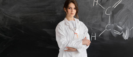 Chemistry teacher or student girl stands against the background of the blackboard with a chemical...