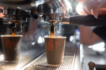 Close-up of a coffee machine making an espresso. The coffee flows into a paper cup under the metal spout of the coffee maker. Production of hot coffee.の写真素材