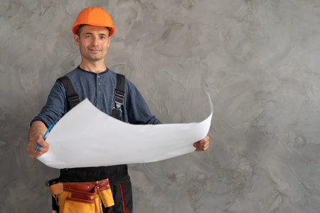 portrait of engineer repairman with house renovation plan in hands on background of concrete wall....