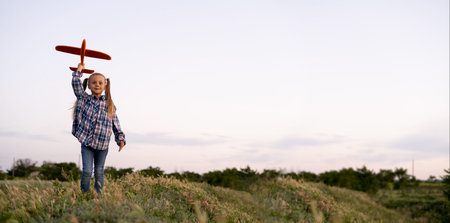 cheerful child girl with a toy airplane walks in the summer field at sunset and launches into the...