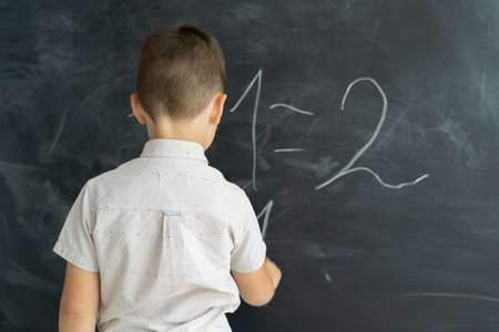 Back view of a student in a class writes chalk numbers on a blackboard. Math lesson. Junior School. Education concept. Back to school. Place for text. copy spaceの写真素材