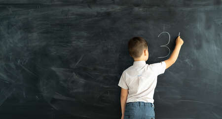 Pupil in class at a math lesson writes on a chalk board with chalk. Elementary school math lesson. Learning concept. Back to school. Banner and place for text.の写真素材