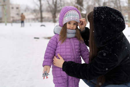 Portrait of a cheerful mother and her daughter in the winter outdoors. A woman straightens a scarf for a child.の写真素材