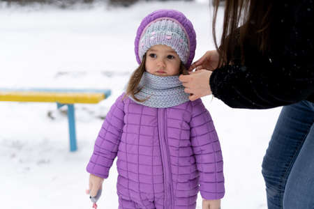 in the winter outdoors a little preschool girl stands on the snow. Mom straightens the babys scarf.の写真素材