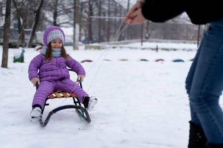 happy child girl in purple jacket having fun outdoors in winter on a sleigh. Healthy excited child sliding down a snowy slope, family winter time.の写真素材