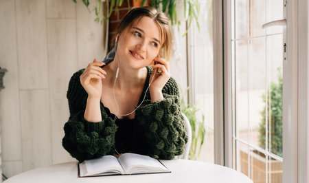 close-up of a girl with a book and headphones in a cafe. Young business lady is resting listening to music while sitting in a cafe in the morning. Relaxation or weekend.の写真素材