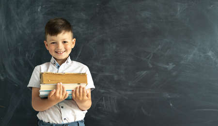 Happy college student standing by the chalk board in the classroom with textbooks or books in hand. Laughing elementary school student. Academic year. Back to school. Banner. Place for text.の写真素材