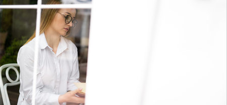 A woman journalist in a cafe by the window looks at notes in a notebook, plans meetings and a working day. Business lady has morning coffee in the cafeteria. lifestyle concept. Banner. place for textの写真素材