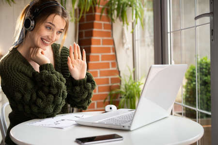 Happy caucasian woman in a wireless headset has a video call on a laptop using a web cam while sitting in a cafe. Chatting or remote teacher online. Digital user and technology concept.copy spaceの写真素材