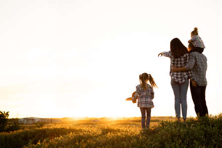 Happy family with two children daughters look at the sunset in the summer. Mom shows her hand to the children at the sky. Motherhood and childhood concept. Parents with girls in nature.の写真素材