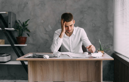 Burnout syndrome at work. Young businessman in stress at workplace with headache unmotivated works...