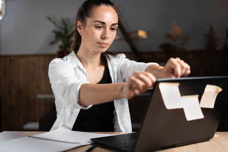 Freelancer girl glues sticky stickers on a laptop while sitting at a home office table. Lack of...