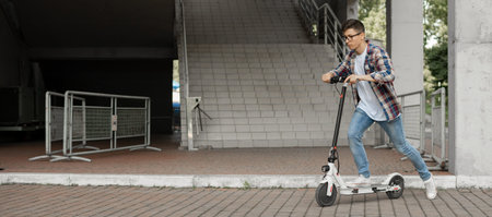 A young businessman in a shirt and glasses starts riding an electric scooter. The modern...