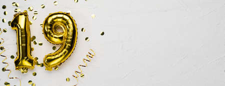 golden foil balloon number nineteen. Birthday or anniversary card with the inscription 19. gray concrete background.の写真素材