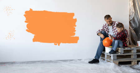 repairing his house and the son are sitting resting near the wall with an orange spot. Baner.の写真素材