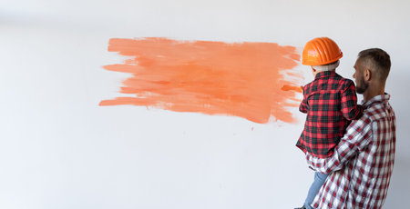 Renovation in the apartment. The father raised his son to paint the wall with a paintbrush. Cheerful...