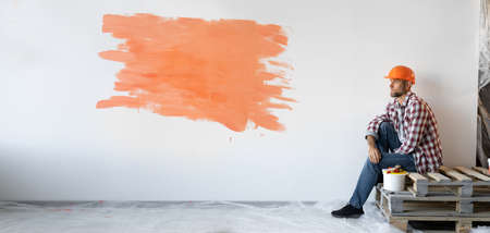 Caucasian man sits on boards near a white wall with an orange spot and a place for text. Baner.の写真素材
