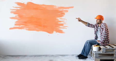 Caucasian man sits on the boards with his forefinger points to an orange spot on the wall.の写真素材