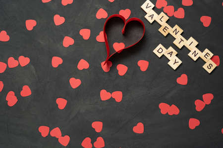 Valentines Day text word wooden blocks with paper hearts on black cement floor with red ribbon. February 14 is a holiday. Winter Valentines Day celebration concept.の写真素材