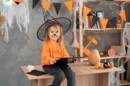 A little girl sits at home on the table and looks at the makeup in honor of the Halloween holiday.の写真素材