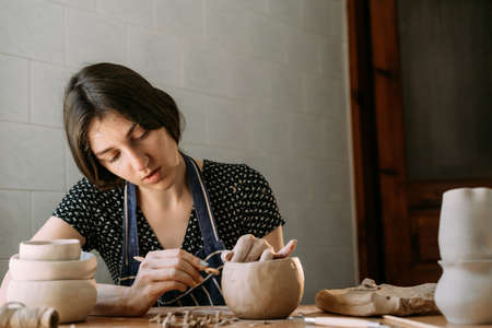 An Armenian girl makes a clay product. Modeling in a home workshop. Creativity and handmade. Clay pot in the hands of a woman with a tool. Art conceptの写真素材