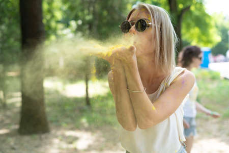 A Caucasian girl at the Holi Festival of Colors blows off the powder of multicolored paint from her hands. Color Fest. Holi celebration conceptの写真素材