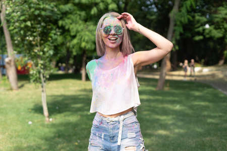 The girl celebrates the Holi festival of colors. ColorFest and a blonde with a face in multi-colored powder paints. Festival in the park and happyの写真素材