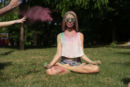 Young woman in the lotus position at the Holi festival meditates in nature powder paint is poured on the girl. Color Fest and outdoor meditation.の写真素材