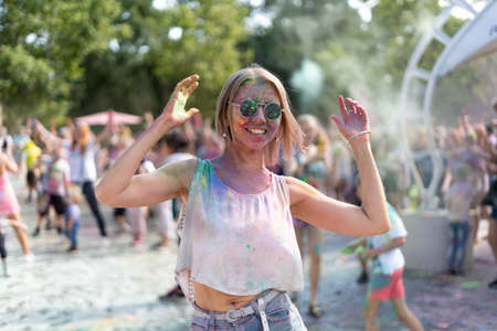 Dancing blonde at the Holi Fest festival in the city park in summer. A colorfest of dry paints and a girl dancing to the music. Birthday party conceptの写真素材