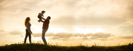Caucasian family mom dad and little son at sunset. Silhouettes of parents and toddler boy on the background of the sky Freedom and an active lifestyleの写真素材