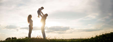 family mom dad and little son walk at sunset. Silhouettes of parents and toddler child on the background of the sky. Freedom and an active lifestyleの写真素材
