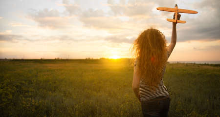 A young girl launches an airplane into the sky while walking in the summer at sunset. Curly woman with a toy in her hands is resting in nature. Dreams of a stewardess about the sky and flight.の写真素材