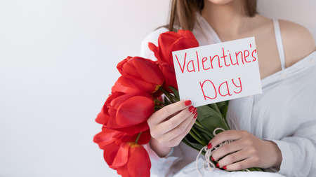 woman holding a bouquet of beautiful red tulips on a white background, Card with the inscription Valentines Day.の写真素材