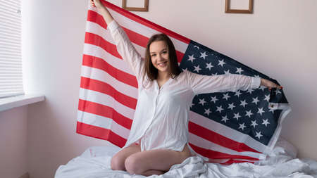 American flag day girl in the bedroom holds the symbol of independence of the united states in her hands behind her back. USA Independence Dayの写真素材
