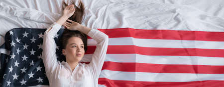 USA Independence Day girl in the bedroom lies on the American flag. young sexy woman celebrating American Flag Day at home on the bed. Banner.の写真素材