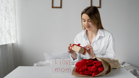 Holiday Mothers Day a woman reads a postcard from a child who gave mom a bouquet of red tulip...