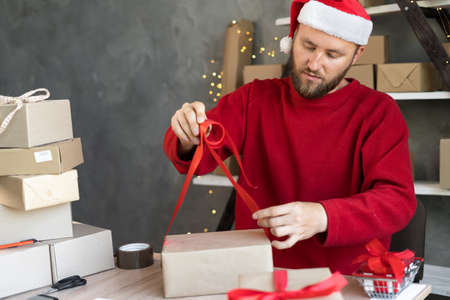 Preparing gifts for Christmas and New Years a man in a Santa hat works in a warehouse preparing an order for goods in boxes for delivery. Saleの写真素材