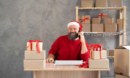 A man in a Santa Claus hat working in a home office takes an order by phone in an online store for delivery on Christmas Day. Owner New Years Sale.の写真素材