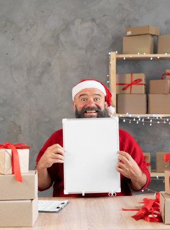 Small business owner a man in a santa hat with a board in his hands sitting at a table in the home office businessman selling goods online store.の写真素材