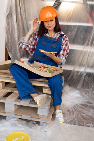Happy millennial girl eating Italian pizza during home improvement of a new house room renovation. Do the repair yourself. Rest and lunchの写真素材