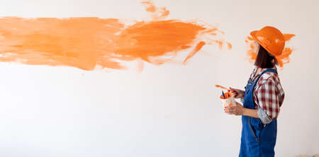 Repair in a new home woman repairman with a brush painted the wall with orange paint. Caucasian girl makes wall decoration in the room. Renovationの写真素材
