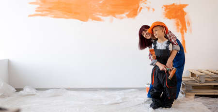 Home repairs. Happy family mom and son painted the wall orange. Wall painting. Renovation or remodel room concept. Woman and child in helmetの写真素材