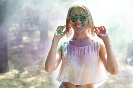 Happy girl with powder paints on face celebrating Holi color festival. Portrait of a young woman in the park at Colorfest. Holi celebration conceptの写真素材