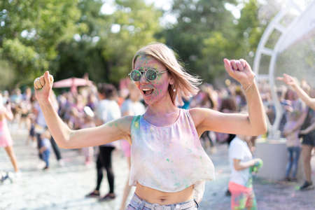Crazy Caucasian girl at Holi Fest festival in city park in summer. A colorfest of dry paints and a blonde dancing to the music. Birthday party conceptの写真素材