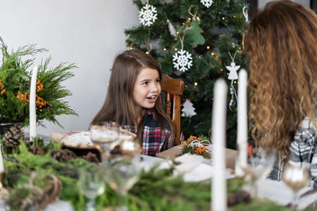 Family mom and daughter have breakfast in the living room for Christmas at a large table decorated with fir candles. Woman giving a gift to a childの写真素材